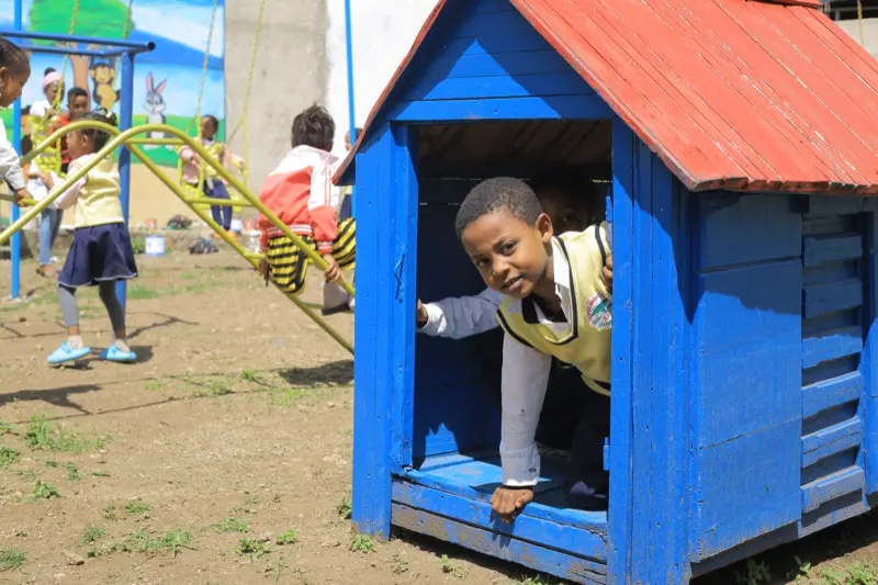 A boy peeks out of a blue wooden playhouse in the KG #1 playground.