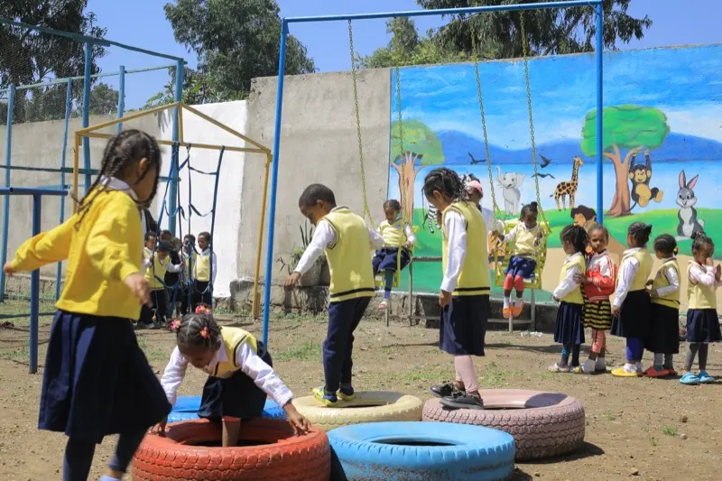 Children climb and balance on painted tyres in front of an animal mural at Keti KG #2.