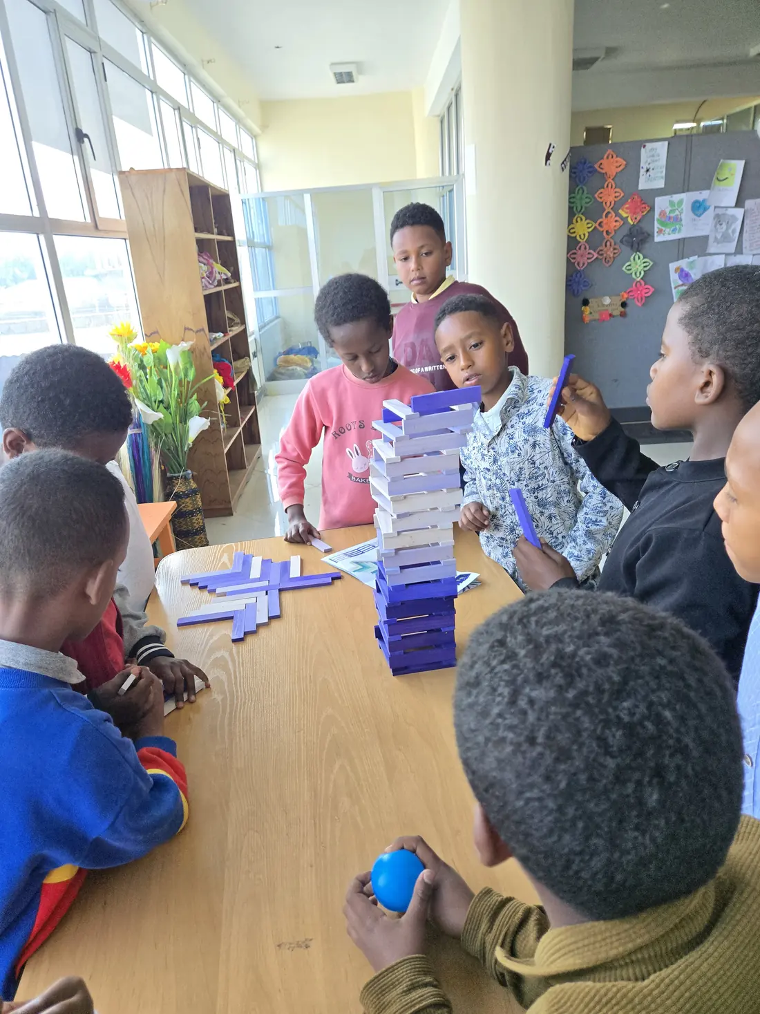 Children play a block-stacking game around a table.