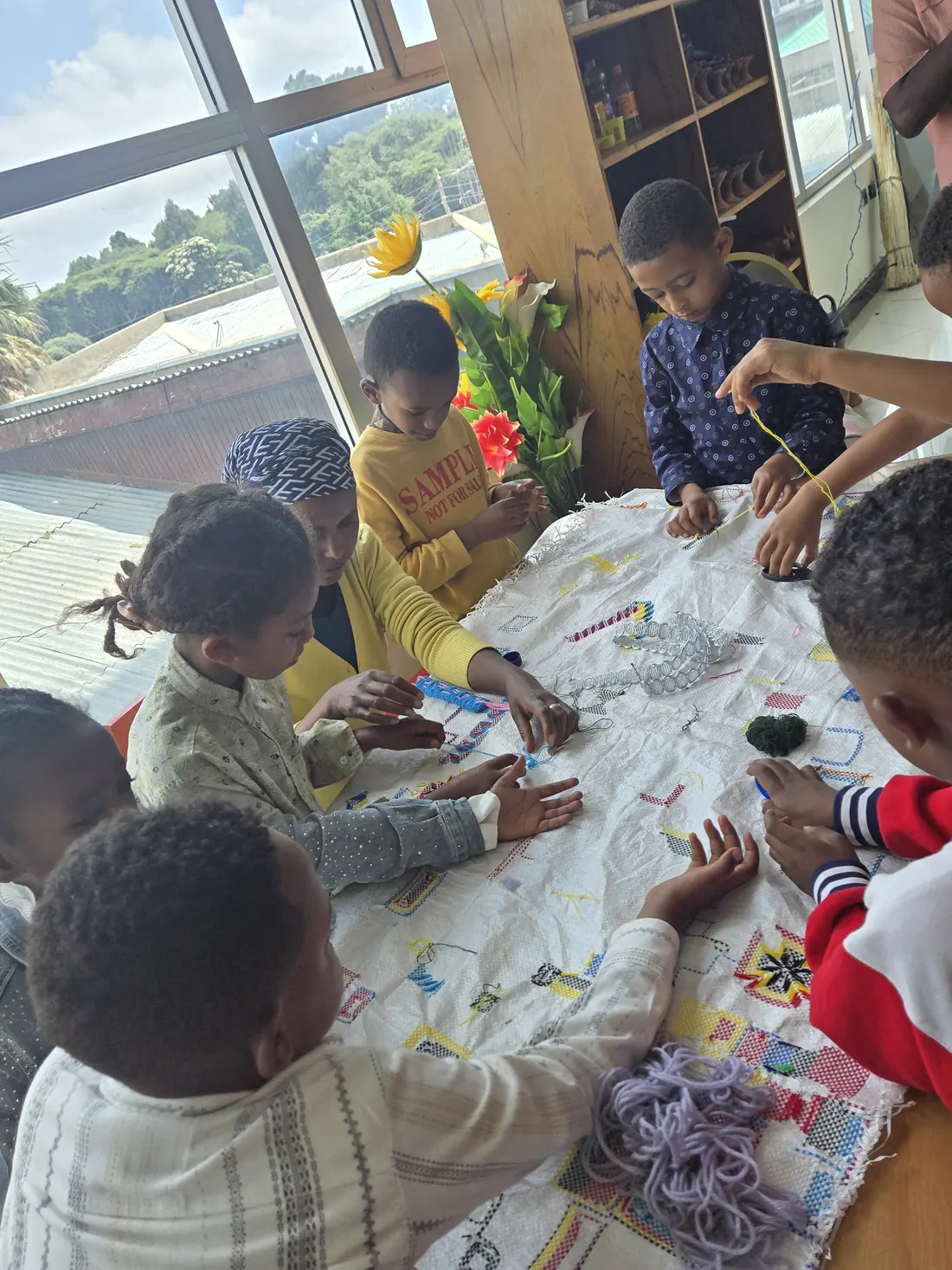 Children work on a big shared craft sheet at a table.