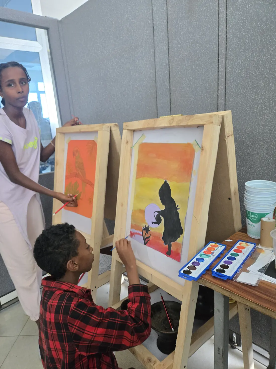 A boy paints a sunset silhouette on an easel.