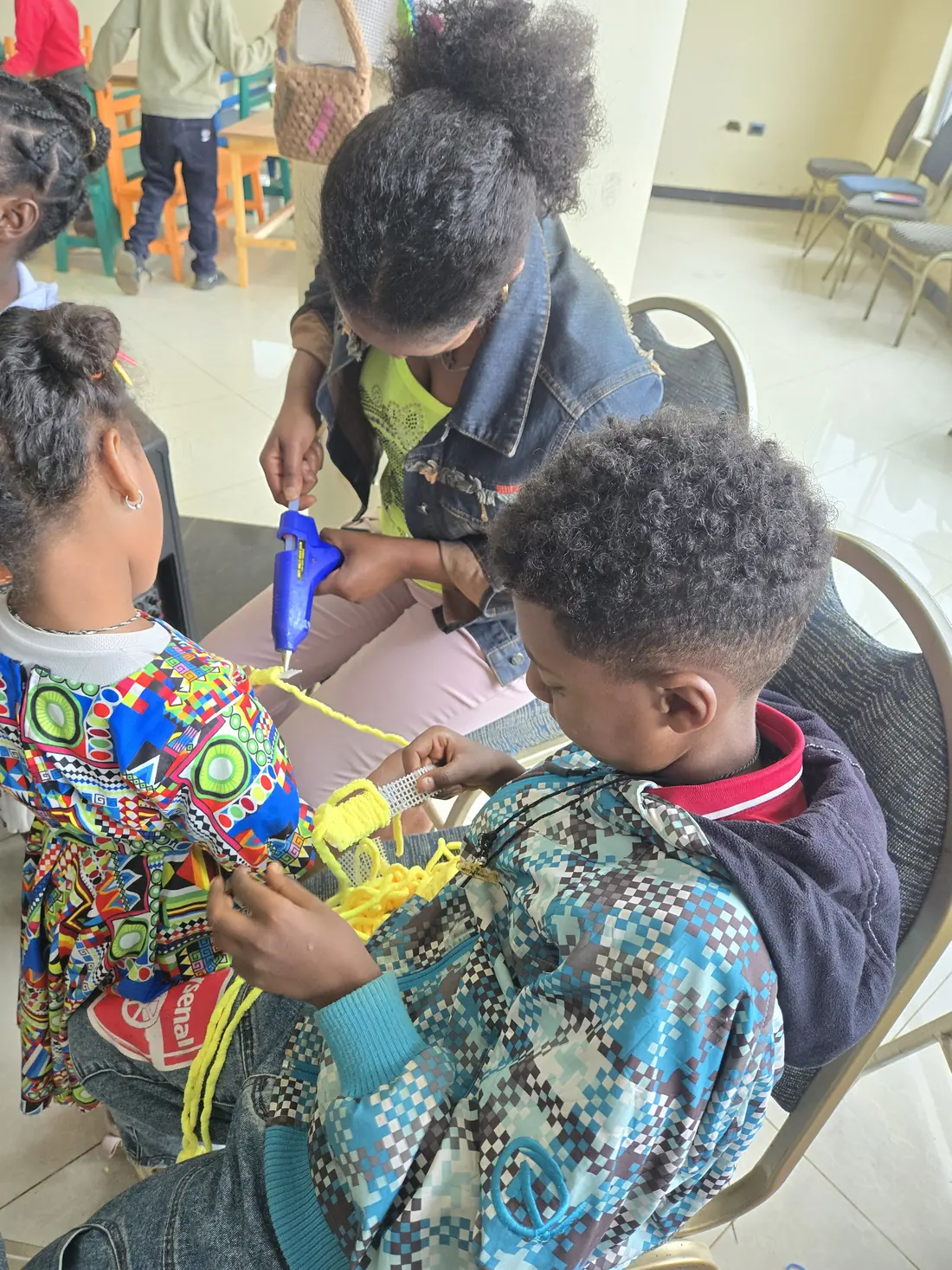 A mother helps children with a craft project using a glue gun.