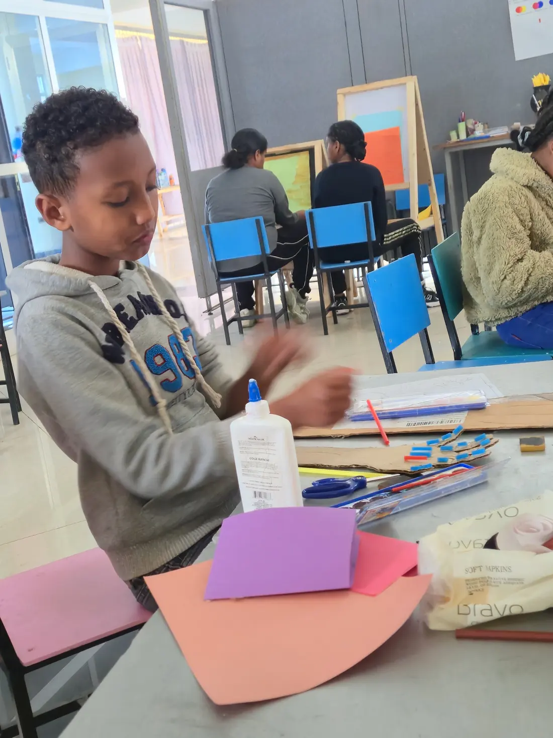 A boy glues coloured paper during a craft session.