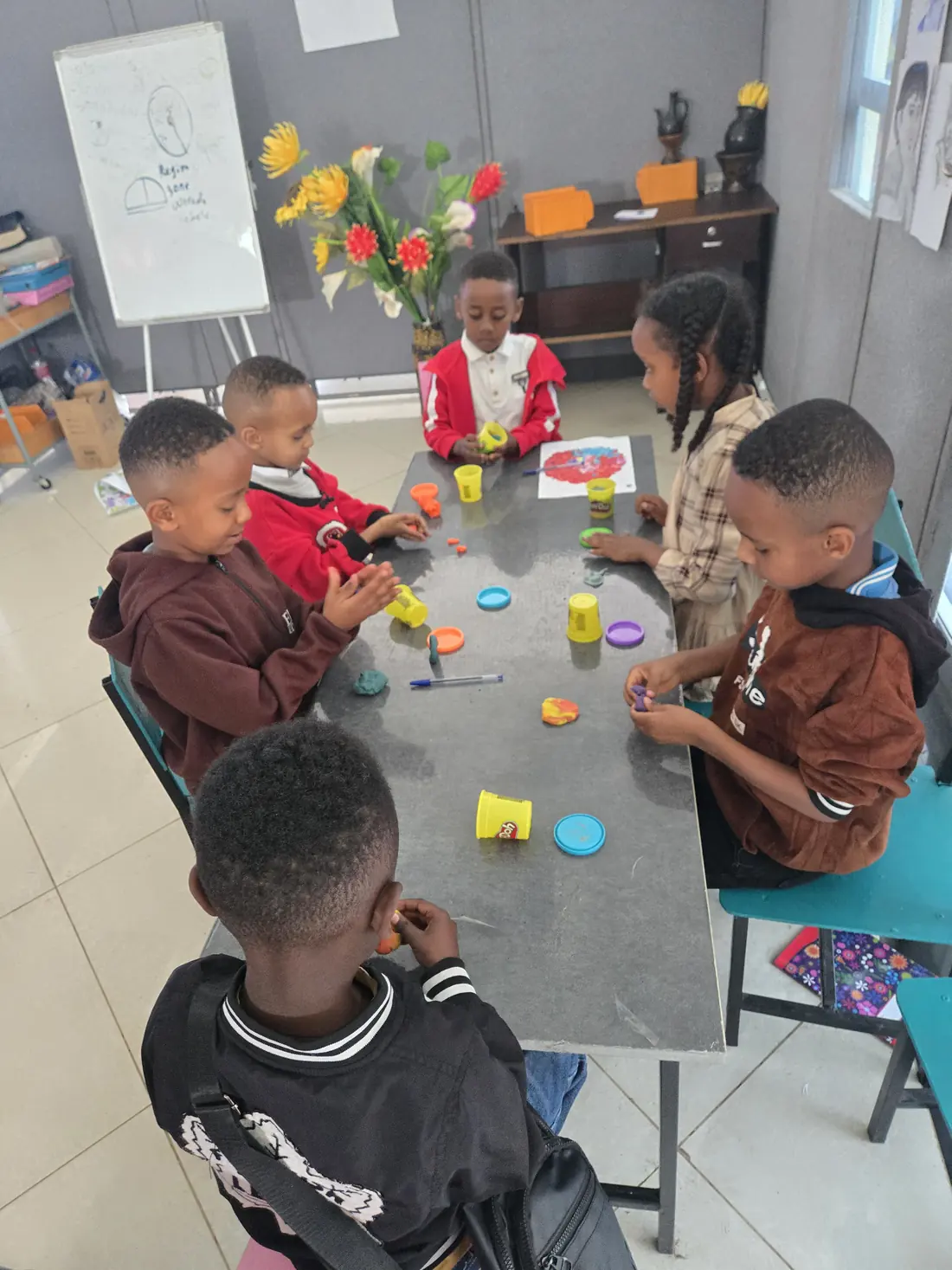 Children shape coloured play dough around a table.
