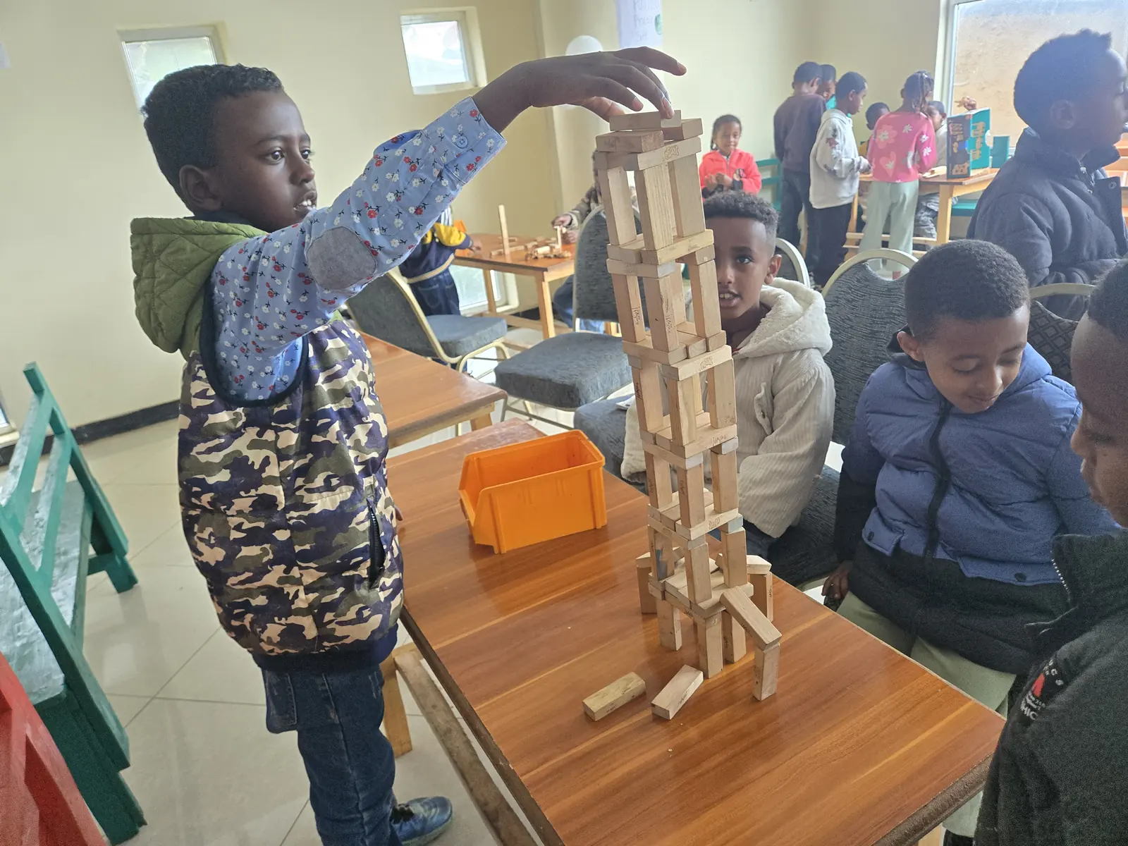 A boy carefully places a block on top of a tall wooden tower.