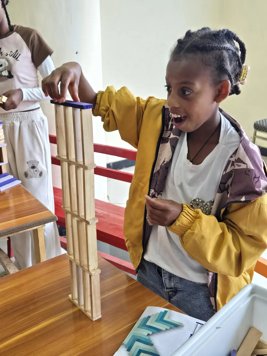 A girl gasps with delight beside her tall block tower.