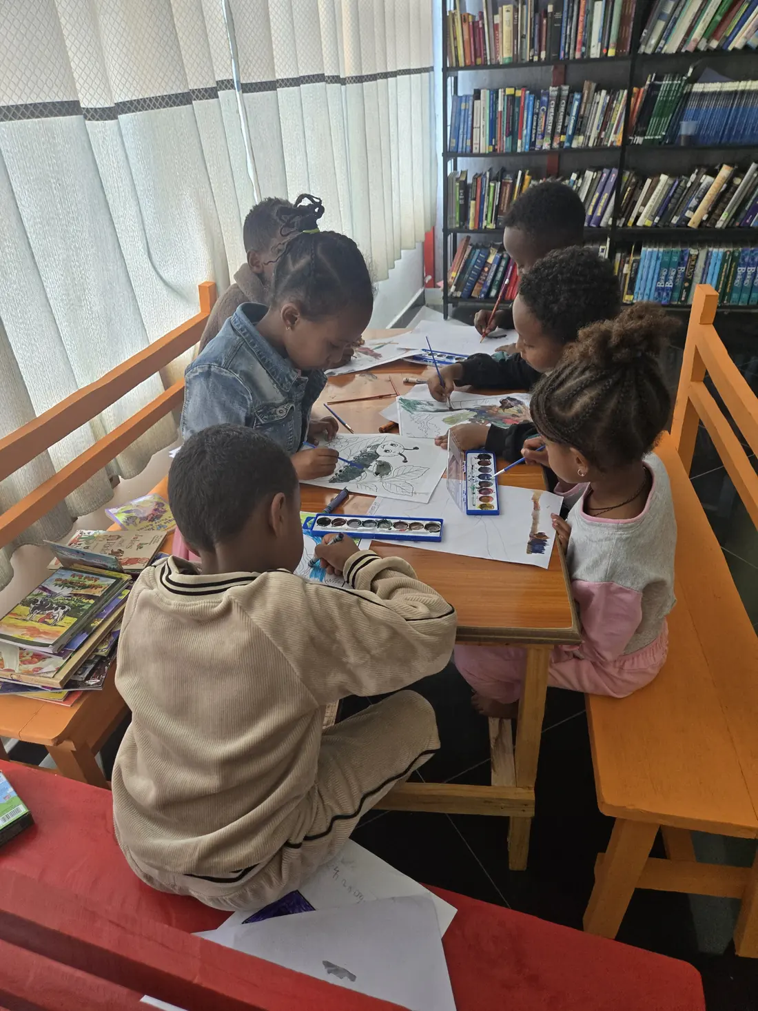 Children paint with watercolours at library tables.