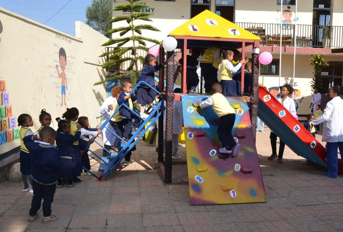 Kindergarten children climb the ladder and climbing wall of the playground frame.