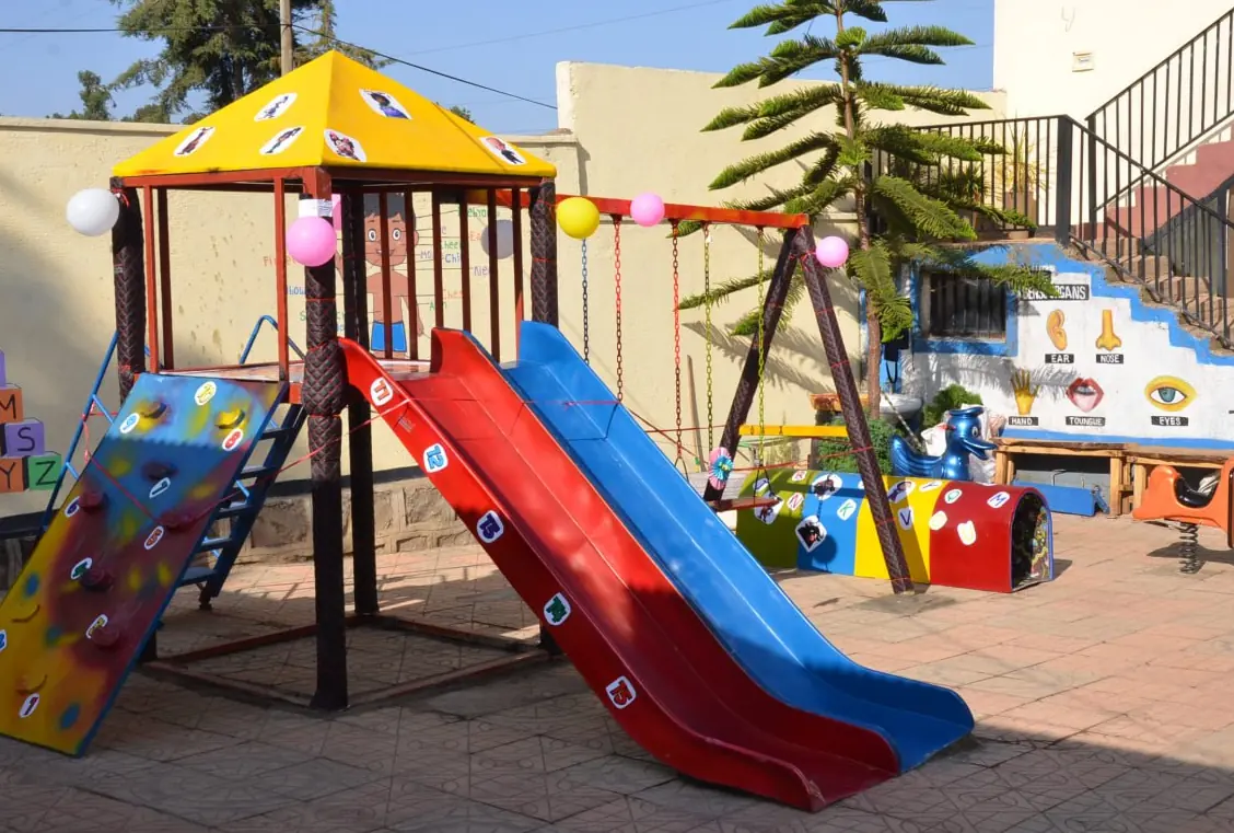 The new KG playground with a yellow-roofed climbing frame, slide and swings, decorated with balloons.