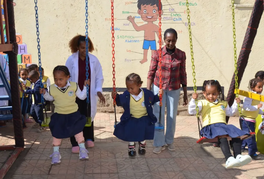 A small girl swings while a teacher and a parent look on.