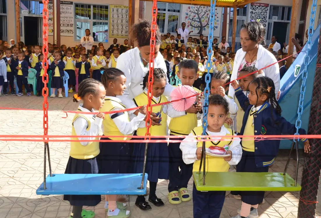 Teachers help young children try the new swings in the KG playground.