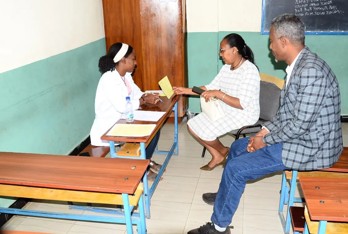 A teacher shares a report with two parents seated at a classroom desk.
