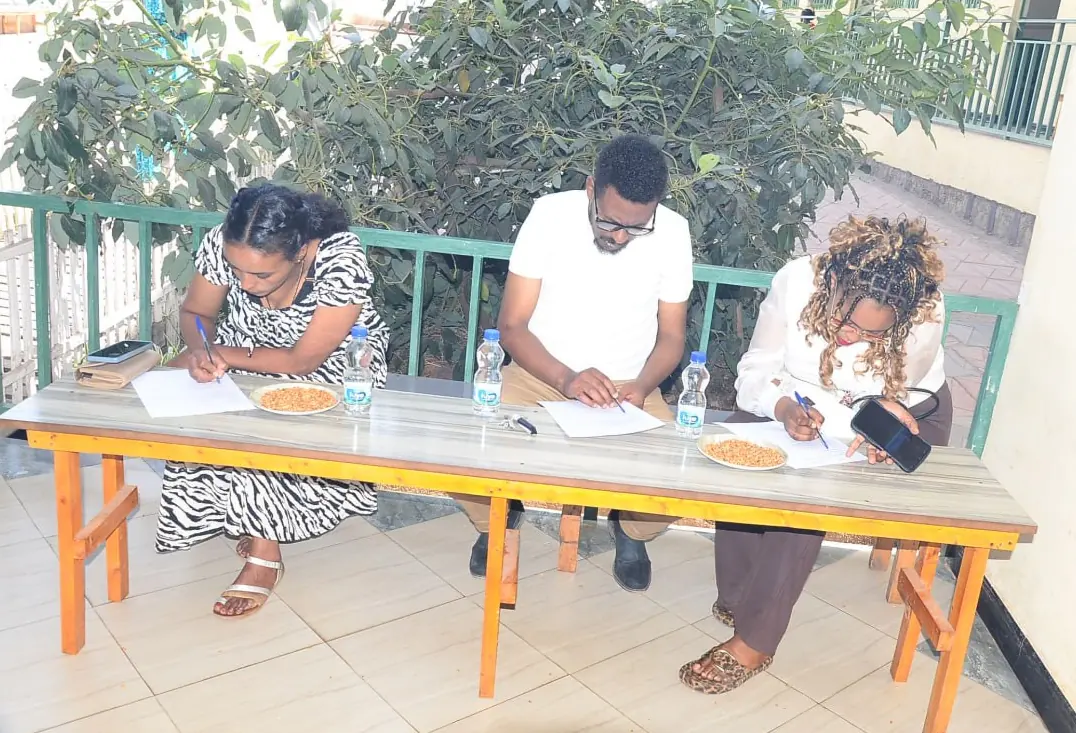 Parents fill in forms at a wooden table on a leafy school balcony.