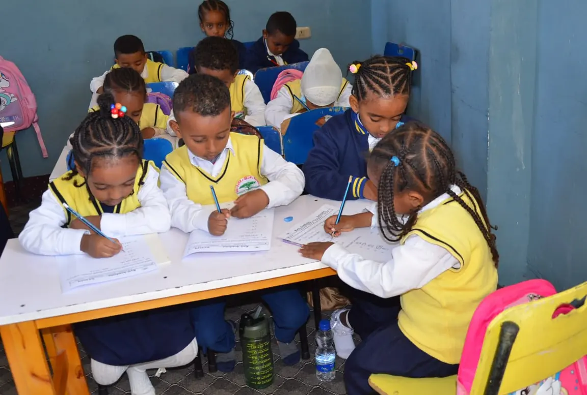 Pupils lean in together over their worksheets at a white table.