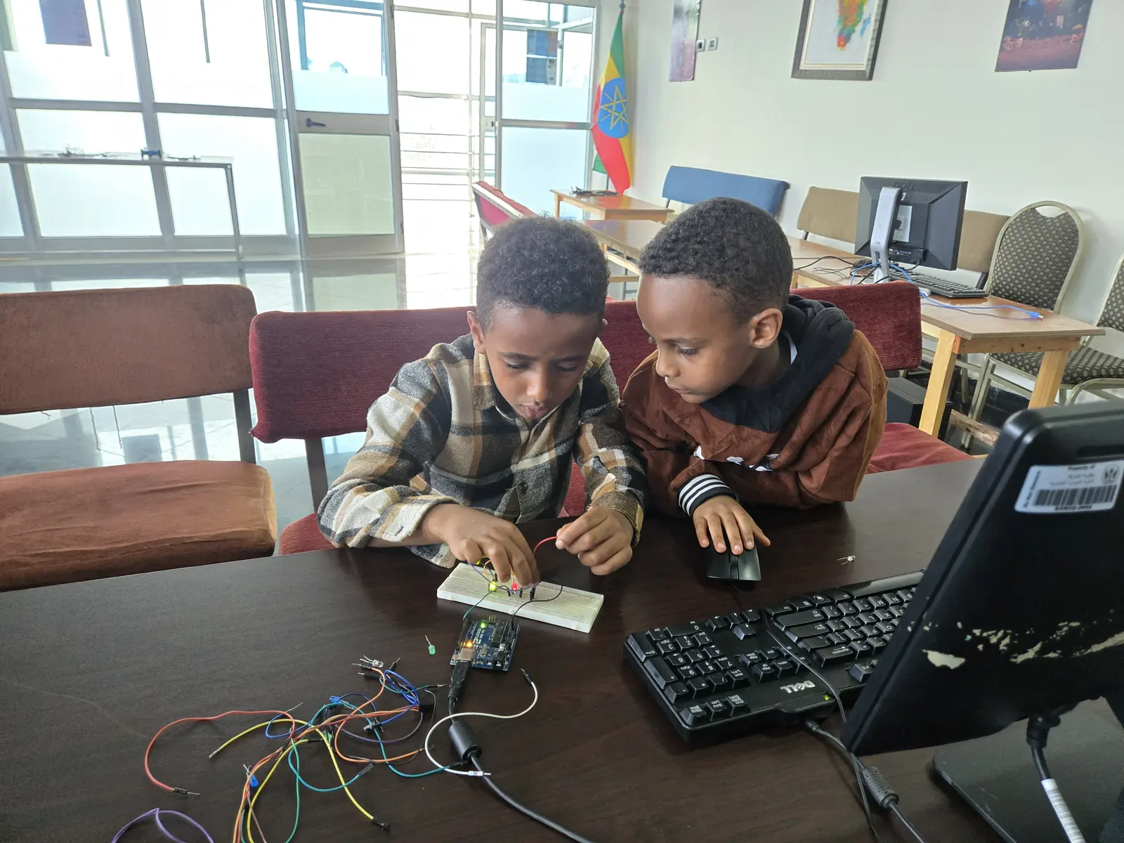 Two boys wire a breadboard circuit at a library computer.